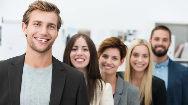 Eine Gruppe aus fünf Personen steht hintereinander und lächelt fröhlich in die Kamera.